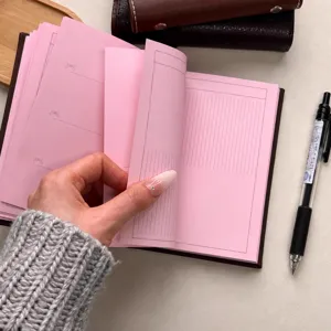 Detailed view of pink inner pages and brown leather cover of A6 notebook for journaling.