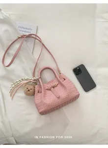Pink woven handbag with top handle, crossbody strap, and cute bear charm for women.