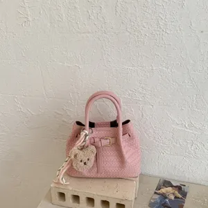 Close-up detail shot of the pink woven bucket bag with a cute plush bear charm and handle.
