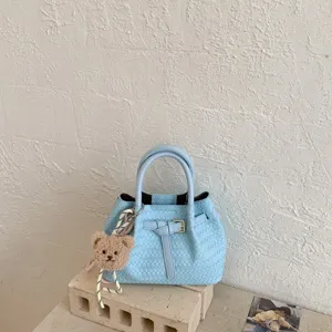 Detailed view of light blue woven leather bucket handbag with cute plush bear keychain charm.