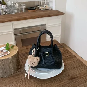 Detail view of black woven leather handbag with elegant buckle and cute bear charm.