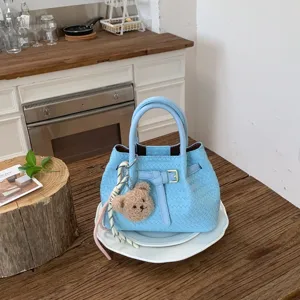 Woven bucket bag detail view, stylish blue handbag with cute bear pendant in a cozy home setting.