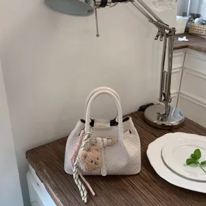 Elegant white woven bucket handbag detail, featuring stylish metal buckle and cute bear charm.