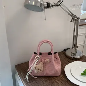 Detail view of pink woven leather handbag bucket bag with cute bear pendant and metal buckle.