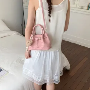 Stylish pink woven crossbody bucket bag for women, versatile summer handbag with cute pendant.