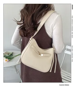 Detailed view of trendy beige shoulder bag worn by model, showing elegant design and hardware.