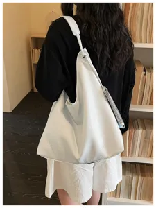 Detail shot of a large white shoulder tote bag worn by model in front of bookshelf.