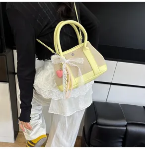 Detailed view of fashionable contrast color canvas leather handbag with cute bow pendant.