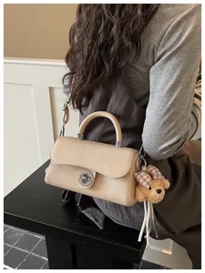 Vista di dettaglio di una borsa beige con chiusura a torsione e ciondolo orsetto.