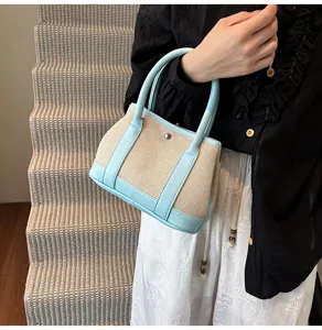 Canvas handbag detail showing light blue leather trim and beige woven fabric texture.