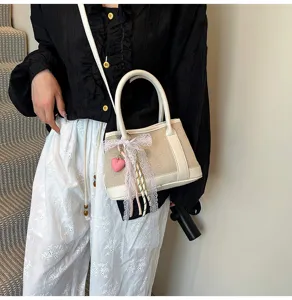 Detail view of the stylish canvas color-block handbag with lace bow and cute heart charm.