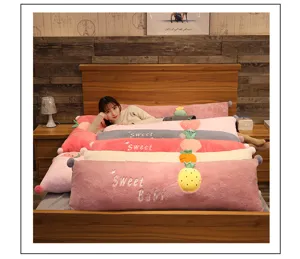 Long plush fruit body pillow with cartoon embroidery and pom-pom decor for bedroom bed.