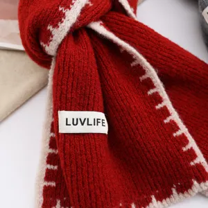 Close-up of red knit winter scarf with white contrast trim and brand label detail.