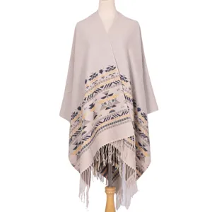 Beige knitted cape shawl with geometric tribal patterns and fringe hem for women.