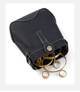 Black leather jewelry storage bag detail showing opening with gold bracelets and rings inside.