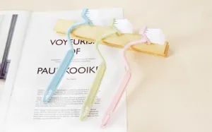 Close-up of curved S-shaped cleaning brush with soft white bristles and long plastic handle.