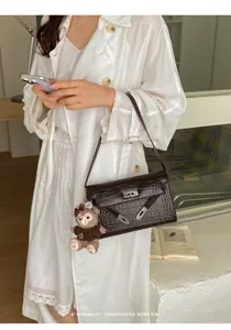 Detailed shot of a chic brown crocodile pattern women shoulder bag with cute bear pendant.