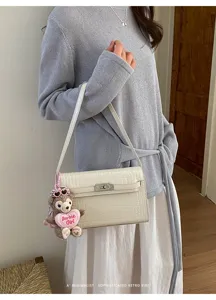 Detailed view of white crocodile texture shoulder bag with cute plush bear keychain accessory.