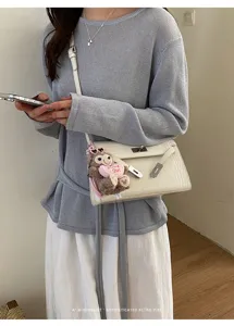 Detailed view of white crocodile embossed shoulder bag with chic plush monkey charm and lock.