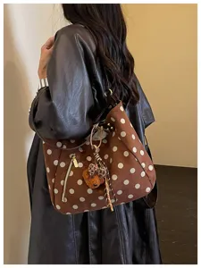 Detailaufnahme der braunen Wildleder-Polka-Dot-Umhängetasche mit Bärenanhänger und Reißverschluss.