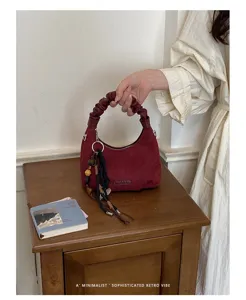 Vue détaillée du sac à bandoulière en suédine rouge sombre avec poignée froncée et pendentif.