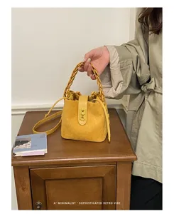 Borsa a secchiello in camoscio stile Maillard, manico intrecciato chic, chiusura in metallo.