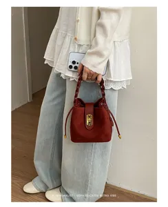 Primo piano di una borsa a secchiello in pelle scamosciata marrone con manico intrecciato.