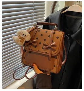 Detail shot of brown polka dot backpack featuring sweet bowknot and cute puppy plush pendant.