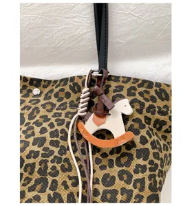 Leopard print tote bag detail showing luxury leather horse charm and sturdy black handle texture.