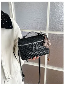 Close-up of black woven vanity bag with flower charm, showing texture and zipper detail.