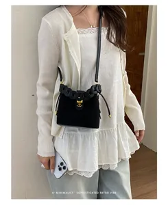 Elegante borsa a secchiello in camoscio con manico intrecciato e chiusura a blocco.