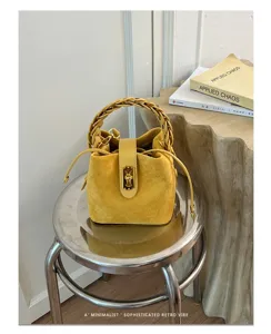 Borsa a secchiello in camoscio giallo con manico intrecciato, chiusura in metallo e coulisse.