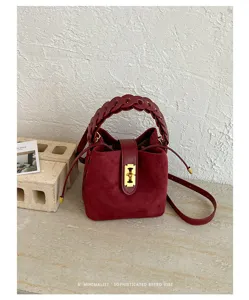 Vista di dettaglio di una borsa a secchiello in camoscio bordeaux con manico intrecciato.