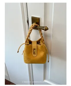 Dettaglio borsa secchiello minimalista in camoscio con manico intrecciato e serratura dorata.