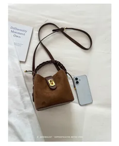 Dettaglio borsa a secchiello in camoscio marrone con manico intrecciato e chiusura dorata.