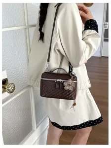 Detail shot of dark brown woven box shoulder bag with flower charm and silver zippers on model.