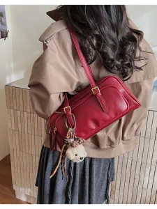 Detail view of stylish red shoulder baguette bag with buckle and cute bear charm accessory.