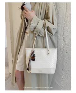 Gedetailleerd shot van een stijlvolle witte geweven tote tas met schouderband en hangers.