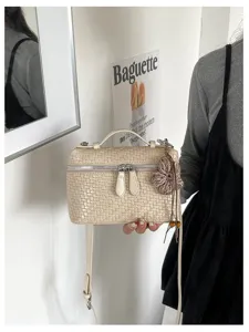 Detail view of beige woven vanity shoulder bag with fringe charm and double zipper closure.