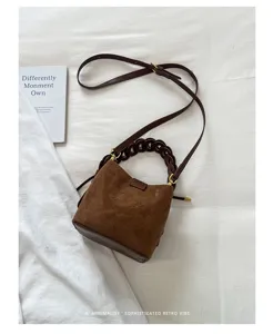Borsa a secchiello in camoscio marrone stile Maillard con manico intrecciato e tracolla.