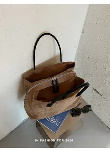 Retro bruine suèdetas met zwarte handvatten en een ruime binnenkant voor dagelijks gebruik.