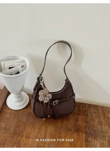 Vista dettagliata della borsa a spalla intrecciata marrone scuro con ciondolo a fiore e fibbia.