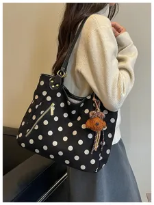 Nahaufnahme der schwarzen Wildleder-Punkte-Tasche mit einem süßen Bärenanhänger an der Schulter.