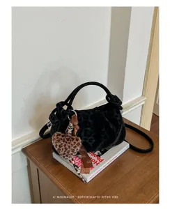 Close-up of stylish black leopard print cloud handbag with cute heart charm and ribbon decor.