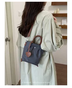 Sac seau en nylon tendance pour femme avec anses marron, bandoulière et charm en forme de cœur.