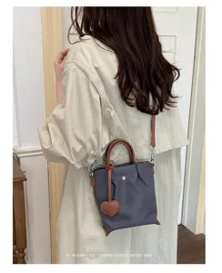 Sac seau minimaliste en nylon avec anses marron et charm cœur sur modèle élégant.