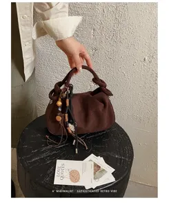 Détail de sac à main froncé en suédine marron, poignée nouée avec charms perlés, style rétro chic.