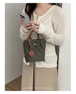 Vue détaillée du sac seau en nylon vert avec poignée en cuir marron et pendentif cœur.