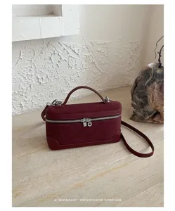 Detail view of wine red suede vanity box bag with metallic zipper in minimal art scene.