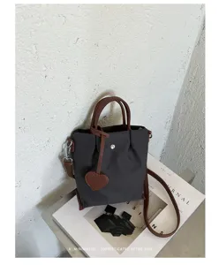 Sac seau bandoulière minimaliste en nylon avec poignées en cuir marron et pendentif cœur.